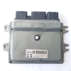 May include: A silver-grey automotive computer module with three black connectors. The module has a label with the Nissan logo, a barcode, and the text "MADE IN JAPAN".
