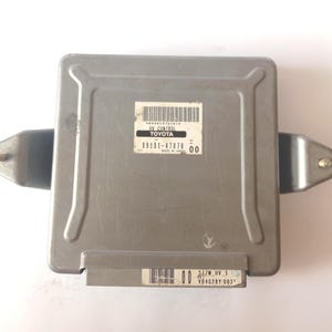 Könnte beinhalten: Ein silbernes Toyota HV Control Modul mit rechteckiger Form. Das Modul hat ein Etikett mit Text und einem Barcode. Es hat zwei Metallhalterungen an den Seiten und einen Anschluss an der Unterseite. Der Text auf dem Etikett lautet "TOYOTA" und "HV CONTROL".