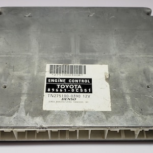May include: A silver engine control unit with a white label that reads "ENGINE CONTROL TOYOTA 89661-0C551 TN275100-0390 12V DENSO MANUFACTURING TENNESSEE, INC."