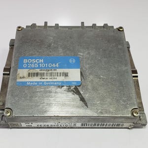 Op de afbeelding: Een zilverkleurige Bosch ABS-regeleenheid met een blauw en wit label. Het label bevat de tekst "BOSCH" en "Made in Germany". De module heeft een rechthoekige vorm met metalen beugels en schroeven.