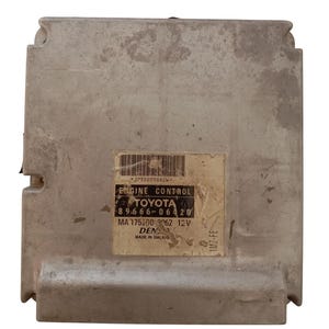 Op de afbeelding: Een zilverkleurige motorbesturingsmodule met een label met de tekst "ENGINE CONTROL TOYOTA". Het label toont ook de nummers "89666-06420" en "MA 175200 9062 12V". De module is gemarkeerd met "DENSO MADE IN MALAYSIA".