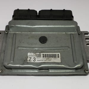 Op de afbeelding: Een zilverkleurige Nissan Z3 motorregeleenheid (ECU). De ECU heeft twee zwarte connectoren aan de bovenkant en een label met tekst en een streepjescode. De unit heeft montagegaten en vinnen aan de zijkanten.