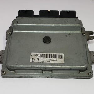 May include: A silver Nissan car computer module with three black connectors. The module is rectangular with mounting tabs and a label stating "MADE IN JAPAN".