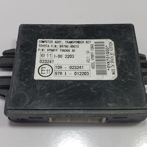 May include: A black computer assembly transponder key with a white label. The label includes text such as "COMPUTER ASSY, TRANSPONDER KEY" and "TOYOTA P/N: 89780-00010". The key has a rectangular shape with protruding side elements.