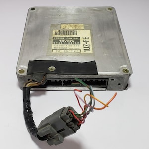 May include: A silver engine control unit with a black label that reads "ENGINE CONTROL TOYOTA 89661-30432 175000-4100 12V DENSO MADE IN JAPAN 26P 16P 22P 1UZ-FE". The unit has a grey connector with multiple wires attached.