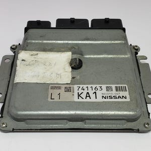 Könnte beinhalten: Ein silberfarbenes elektronisches Steuergerät (ECU) mit schwarzen Anschlüssen. Das Steuergerät hat eine rechteckige Form mit Befestigungslaschen und einem Etikett mit der Aufschrift "741163 KA1 NISSAN".