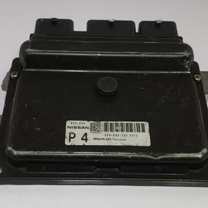 May include: Black Nissan P4 electronic control unit (ECU). The ECU has three black connectors on top and a label with a barcode and text. The unit has mounting brackets on the sides and is likely for an automobile.