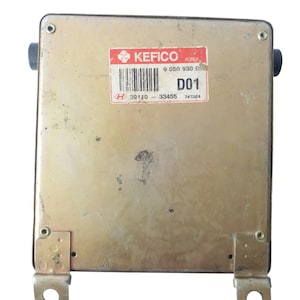 Puede incluir: Una pieza automotriz rectangular de color metálico con una etiqueta roja y blanca que dice "KEFICO" y "D01". La pieza tiene soportes de montaje y componentes de goma negra. La etiqueta también incluye un código de barras y los números "9 050 930 05" y "39110 - 33455".