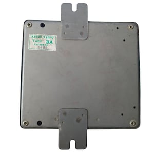 Pode incluir: Um componente eletrónico retangular prateado com dois suportes metálicos e um autocolante. O autocolante tem texto verde e branco, incluindo os números "33920 71EFO 71EF 3A" e "E2T48871 5408".