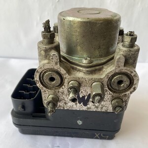 Op de afbeelding: Een gebruikt, metallic zilver en zwart auto-onderdeel. Het onderdeel heeft meerdere poorten, schroeven en een cilindrische bovenkant. Op het onderdeel staat de letter "W". Het is waarschijnlijk een ABS-module of een vergelijkbaar onderdeel.