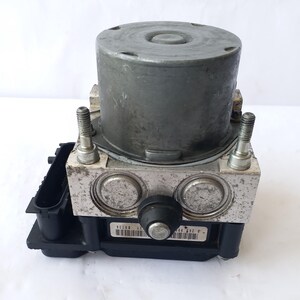 Op de afbeelding: Een metallic grijs auto-onderdeel met een cilindrische bovenkant en een rechthoekige basis. Het onderdeel heeft twee zilveren bouten, twee cirkelvormige componenten en een zwarte kunststof component. Een barcode-sticker is zichtbaar aan de voorkant.