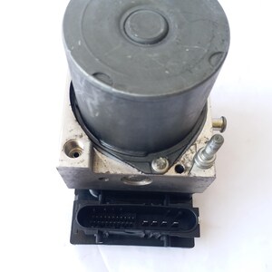 Op de afbeelding: Een cilindrische, grijze metalen component met een zwarte rechthoekige connector aan de basis. De component heeft een cirkelvormige bovenkant en een zilverkleurige bout die uit de zijkant steekt. De basis is van zilverkleurig metaal.