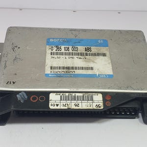 Op de afbeelding: Een zilverkleurige ABS-regeleenheid met een zwarte connector en montagebeugels. De module heeft een blauw en wit label met de tekst "BOSCH" en andere nummers en codes. Gemaakt in Duitsland.