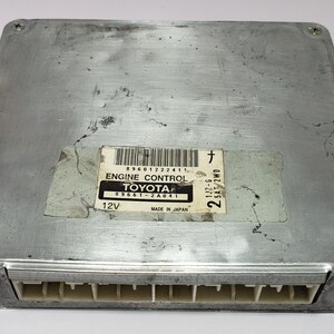 May include: A silver engine control unit with a black label that reads "TOYOTA ENGINE CONTROL 89661-2A041 12V MADE IN JAPAN" and a white label with the number "8960122411" and the text "2 1125 5A/7.2WD".