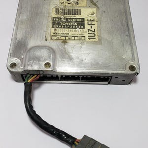 May include: A silver engine control unit with a black wire harness and a grey connector. The unit has a label that reads "ENGINE CONTROL TOYOTA 89661-30430 75000-2403? DENSO MADE IN JAPAN 26P 16P 22P 1UZ-FE".
