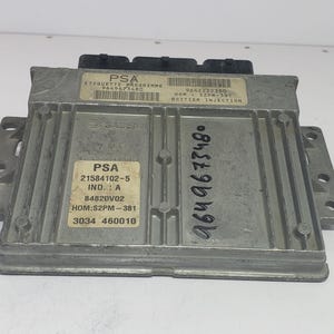 May include: A silver-colored automotive computer module with multiple labels and connectors. The labels include text such as "PSA", "ETIQUETTE PROGRAMME", and various numerical codes. The module has a rectangular shape with mounting brackets on the sides.