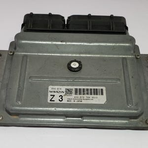 Può includere: Centralina motore Nissan Z3 color argento con connettori neri. Il modulo ha un'etichetta con testo e codice a barre. Made in Japan è stampato sull'etichetta. Ha linguette di montaggio e alette di raffreddamento.
