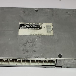 以下が含まれることがあります： 「ENGINE CONTROL TOYOTA 89666-28130 211000-8530 12V 1A2F5 AT」と表示されたラベルが付いた銀色のエンジンコントロールユニット。