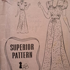 Op de afbeelding: Vintage naaipatroon voor een jurk met bloemenprint. Het patroon bevat illustraties van de jurk, de tekst "SUPERIOR PATTERN" en de naam "Cynthia Powell". Het logo van Sears Roebuck and Co. is ook zichtbaar.