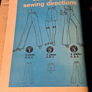 Puede incluir: Un sobre de patrón de costura vintage Simplicity 8289 con un panel rectangular azul e ilustraciones de líneas negras de tres estilos diferentes de pantalones y shorts. El texto dice Simplicity 8289 cutting and sewing directions.