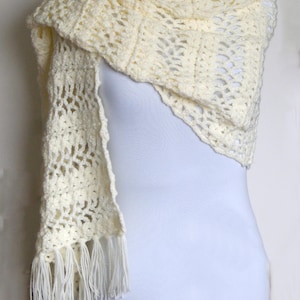 May include: A white crocheted shawl with a delicate openwork pattern and fringe trim.