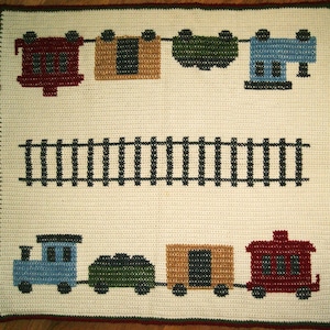Könnte beinhalten: Eine gehäkelte Zugdecke mit zwei Zügen, jeder mit einem roten, blauen, grünen und braunen Wagen. Die Züge fahren auf einem schwarzen Gleis vor weißem Hintergrund.