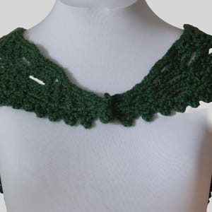May include: A green crocheted collar with a delicate lace pattern. The collar is made of yarn and has a scalloped edge.