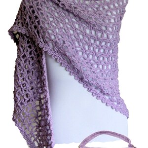 May include: A lavender crochet shawl draped over a white mannequin, with a matching crochet handbag. The shawl has an open, lacy design with a scalloped edge. The handbag features a flap closure and wooden toggle.