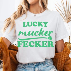 May include: White t-shirt with the words "LUCKY mucker FECKER" in green, with a green shamrock. The shirt is being worn with denim shorts and a mustard-colored cardigan.