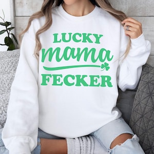 May include: White sweatshirt with the text "LUCKY mama FECKER" in green lettering. The word "mama" is underlined with a green line, and a green shamrock is next to the line. The sweatshirt is worn by a person.