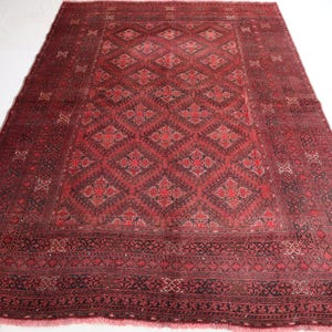 Pode incluir: Um tapete grande, retangular, tecido à mão, com uma paleta de cores vermelho escuro e preto. O tapete apresenta um intrincado padrão geométrico no centro, rodeado por uma borda detalhada. É exibido em uma superfície branca.