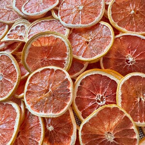 May include: A close-up shot of numerous dried grapefruit slices. The slices are a vibrant reddish-orange color with a pale yellow rind. The arrangement is dense, showcasing the texture and detail of the dehydrated fruit, perfect for culinary or decorative use.