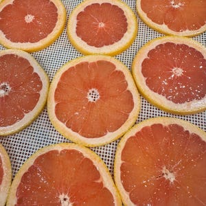 May include: Overhead shot of several sliced grapefruits. The grapefruit slices are arranged in a grid pattern, showcasing their vibrant pink flesh and yellow rinds. The slices are fresh and juicy, with a glistening appearance.