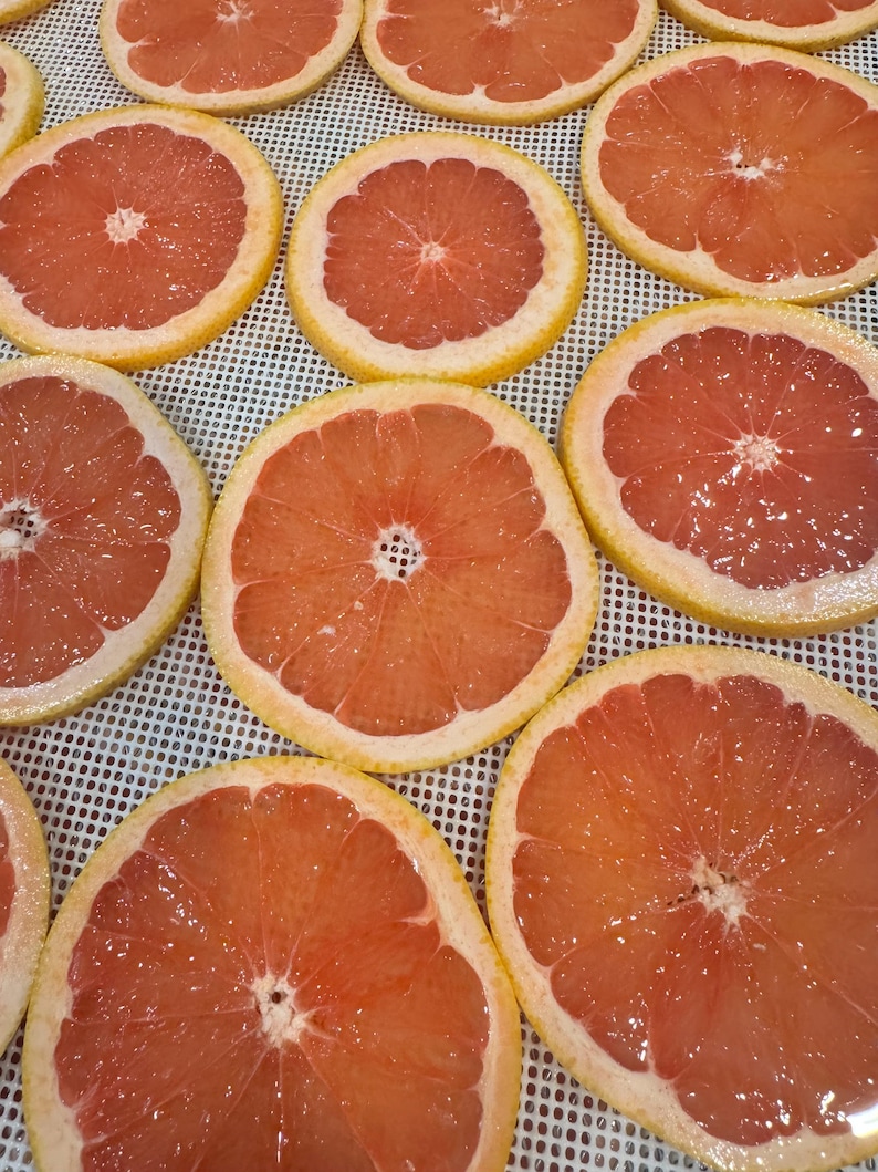 May include: Overhead shot of several sliced grapefruits. The grapefruit slices are arranged in a grid pattern, showcasing their vibrant pink flesh and yellow rinds. The slices are fresh and juicy, with a glistening appearance.