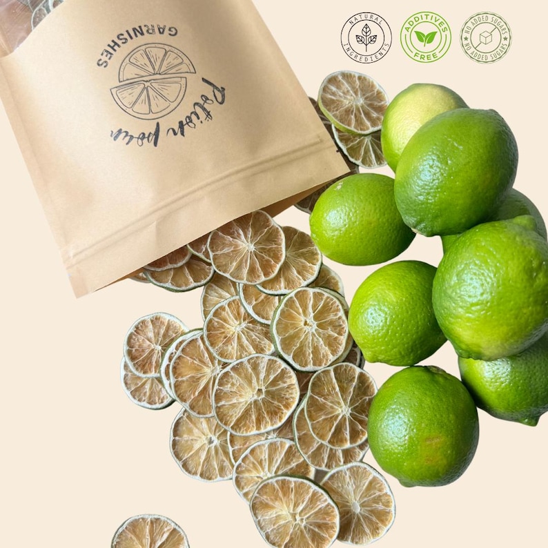 May include: A kraft paper bag labeled "GARNISHES" and "Potion pour" spills dried lime slices. Fresh green limes are clustered nearby. The image also features three circular icons indicating natural ingredients, additive-free, and no added sugars.