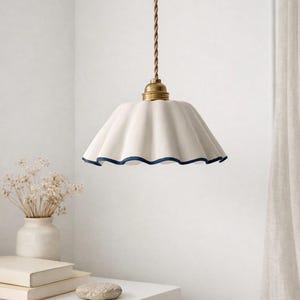 Peut inclure: Suspension en céramique blanche avec bord festonné et bordure bleu marine. La lampe est suspendue à un cordon marron et à un luminaire en laiton. Un élément de décoration intérieure.