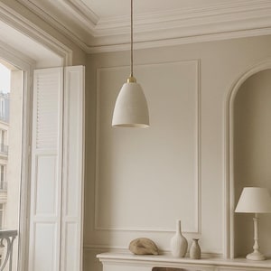 Puede incluir: Una lámpara colgante con una pantalla en forma de campana de color crema cuelga de un cable marrón. La lámpara está suspendida de un techo decorativo. La habitación cuenta con una mesa redonda, una silla y una lámpara pequeña.
