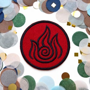 May include: A circular embroidered patch featuring a red background with a black stitched flame symbol in the center. The design is enclosed by a thick black border, creating a distinct emblem with a textured fabric surface.