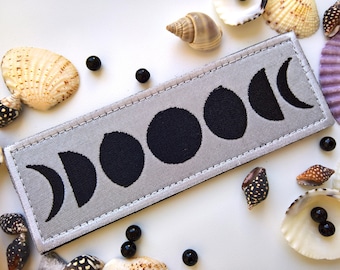 Könnte beinhalten: Ein grauer Stoff-Patch mit schwarzen gestickten Mondphasen. Der Patch hat einen weißen Rand und ist mit weißem Garn gestickt.