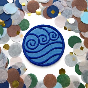 May include: A circular embroidered patch featuring a blue water wave symbol with three stylized swirls above two wavy lines, surrounded by a scattered collection of small, multicolored paper circles in shades of blue, green, brown, and gold.