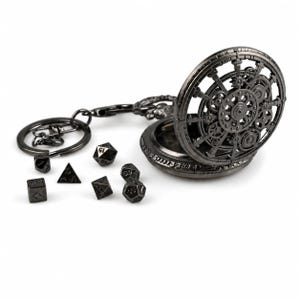 Könnte beinhalten: Ein dunkelmetallischer Schlüsselanhänger mit einem kreisförmigen, durchbrochenen Zahnraddesign, das an eine Taschenuhr erinnert, begleitet von sechs kleinen, mehrseitigen schwarzen Würfeln mit weißen Zahlen, darunter d4, d6, d8, d10, d12 und d20.