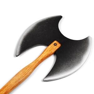 Könnte beinhalten: Eine Doppelaxt mit einem großen, symmetrischen, mattschwarzen Kopf mit silberfarbenen Kanten und einem geschwungenen, hellbraunen Holzstiel. Der Axtkopf ist mit einem einzelnen sichtbaren Metallbefestigungselement am Stiel befestigt.