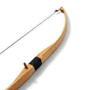 Puede incluir: Un arco recurvo fabricado en madera de color claro con veta visible. La sección de la empuñadura presenta un agarre envuelto en negro y un pequeño reposaflechas de madera que sobresale por el lateral. Una cuerda fina y oscura está sujeta.