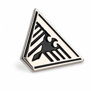 Könnte beinhalten: Eine dreieckige Metallnadel mit polierter silberfarbener Oberfläche und eingelassener schwarzer Emaille. Das Design zeigt ein stilisiertes Vogelemblem mit ausgebreiteten Flügeln und spitzem Schwanz, zentriert im dreieckigen Rahmen.
