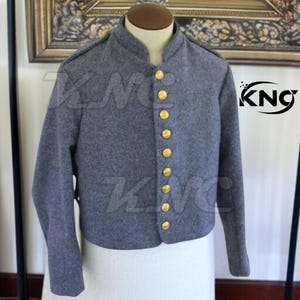 以下が含まれることがあります： グレーのウールジャケット。スタンドカラーと長袖が特徴です。前面には8つの金色のボタンが並んでいます。マネキンに着せられており、歴史的またはミリタリースタイルのアパレルであると考えられます。