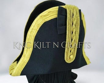 Puede incluir: Un sombrero bicornio negro con ribete dorado y un cordón de hombro trenzado dorado. El sombrero tiene un ala curva y un botón decorativo. El texto "KNC KILT N CRAFTS" es visible en el lateral del sombrero.
