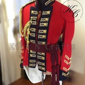 Może przedstawiać: Czerwona kurtka w stylu wojskowym z złotymi guzikami i czarnymi lamówkami. Kurtka ma wysoki kołnierz i pasek. Kurtka jest na manekinie.