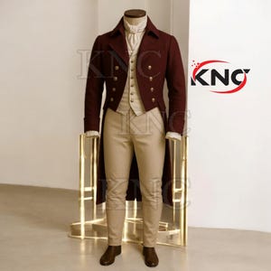 Puede incluir: Un traje de frac burdeos con chaleco crema, camisa y pantalones color beige. El abrigo cruzado tiene botones dorados. El atuendo se exhibe en un maniquí. Es un disfraz histórico.