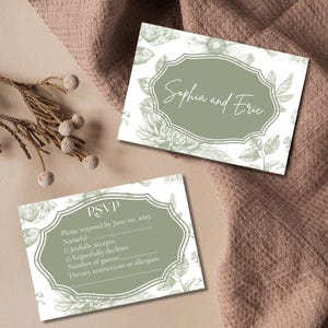 May include: A white RSVP card with green floral designs and text that reads "RSVP Please respond by June 1st, 2025 Name(s) Joyfully accepts Regretfully declines Number of guests Dietary restrictions or allergies" and a separate card with green floral designs and text that reads "Sophia and Eric"