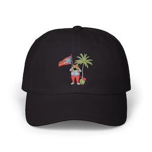 Puede incluir: Gorra de béisbol negra con un diseño bordado. El diseño presenta un personaje de dibujos animados sosteniendo una bandera, de pie junto a una palmera y una sandía. La bandera tiene colores rojo, blanco y azul.